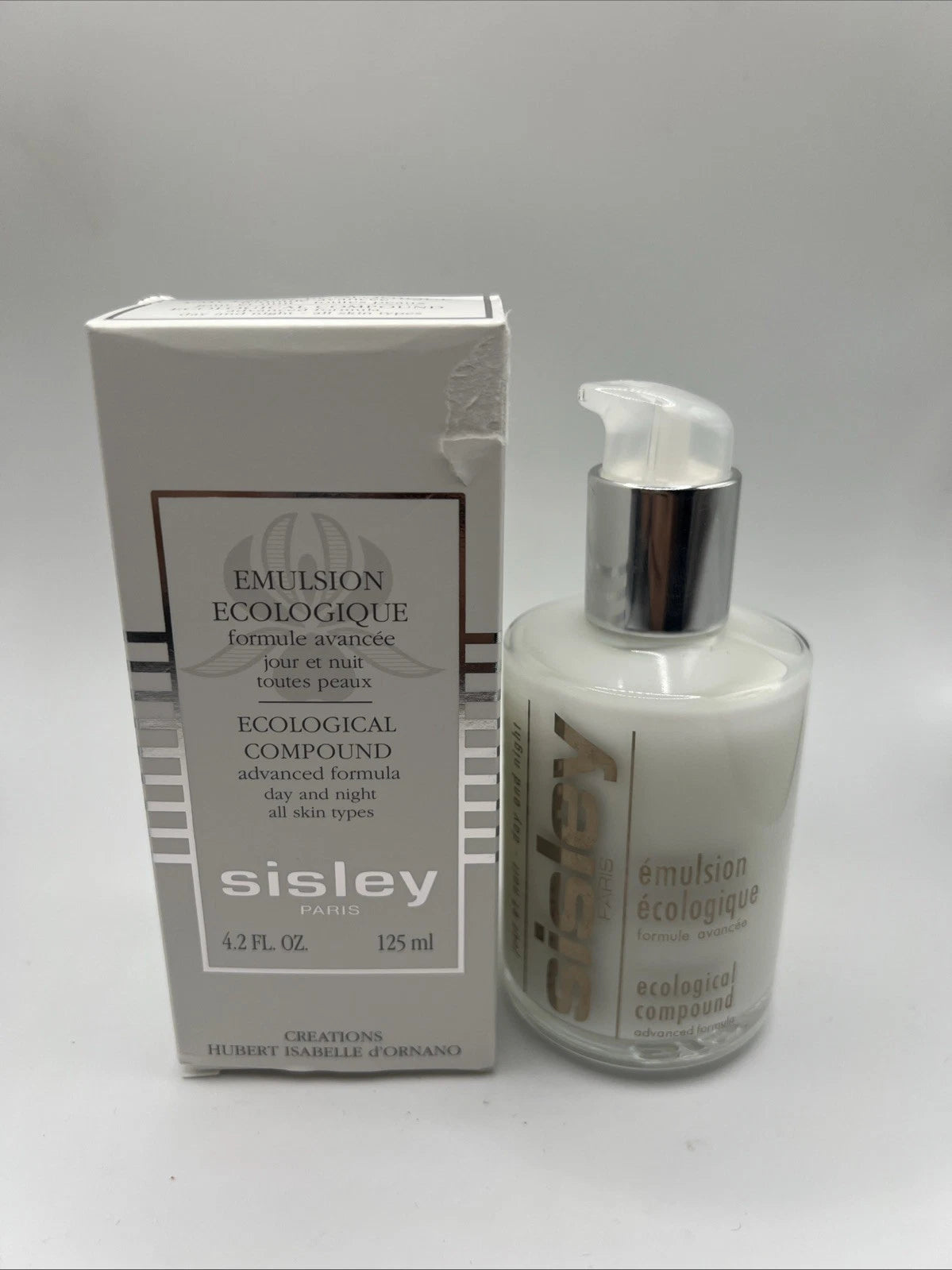 Sisley Emulsion Ecologique emulsion bottle with pump next to its original white packaging box, on a neutral light gray background.
